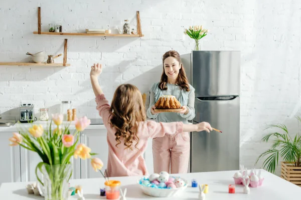 Вид сзади ребенка рядом со счастливой мамой с съедобным тортом — стоковое фото