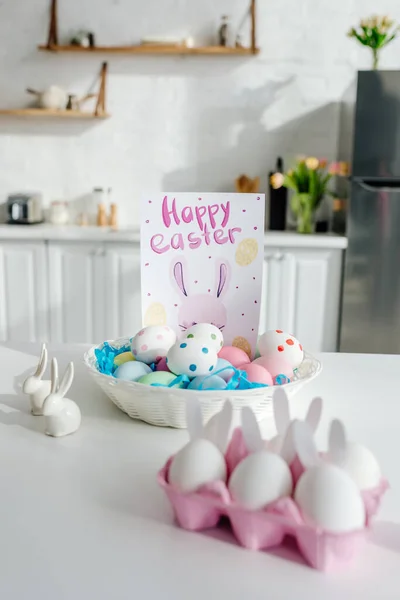 Foco seletivo de ovos de galinha pintados perto de coelhos decorativos e cartão de saudação com letras felizes da Páscoa — Fotografia de Stock