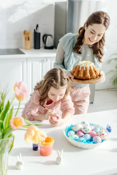 Селективное внимание ребенка живописи куриное яйцо и мать с пасхальным тортом — стоковое фото