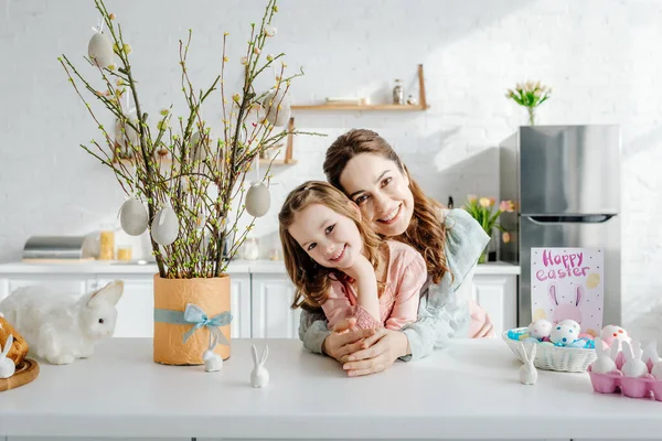 Mãe feliz e filha perto de salgueiro, ovos de Páscoa e coelhos decorativos — Fotografia de Stock