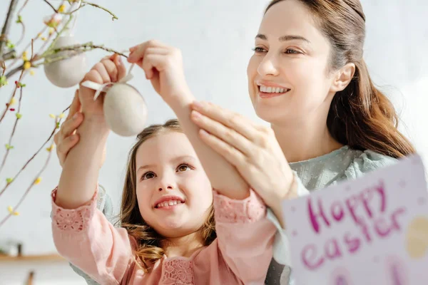 Selective focus of smiling mother and daughter looking at decorative easter eggs — Stock Photo