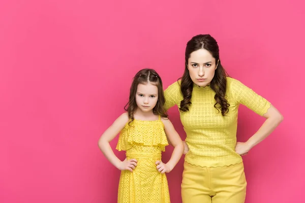 Madre e hija serias de pie con las manos en las caderas aisladas en rosa - foto de stock