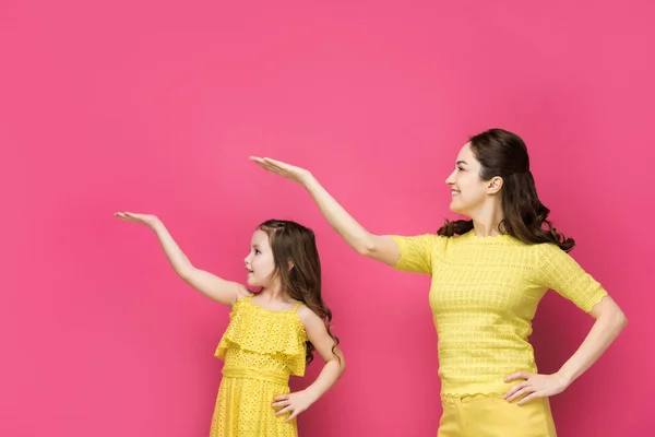 Vista lateral de la madre y la hija señalando con las manos aisladas en rosa - foto de stock