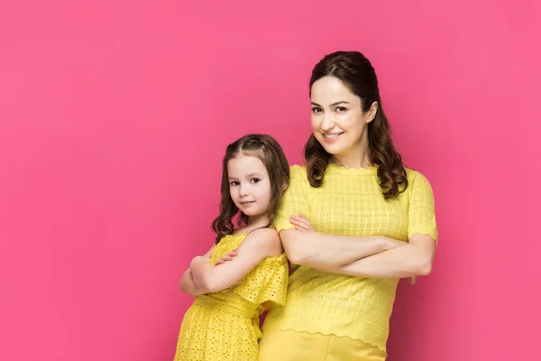 Mujer feliz y niño de pie con los brazos cruzados aislados en rosa - foto de stock