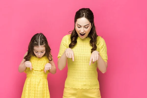 Donna felice e bambino sorpreso che punta con le dita mentre guarda giù isolato sul rosa — Foto stock