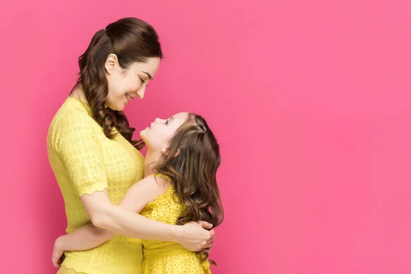 Profile of cheerful mother and daughter hugging isolated on pink — Stock Photo
