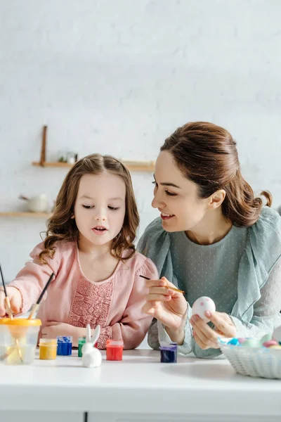 Fuoco selettivo di uova di Pasqua dipinte vicino a coniglietto decorativo, madre felice e figlia — Foto stock