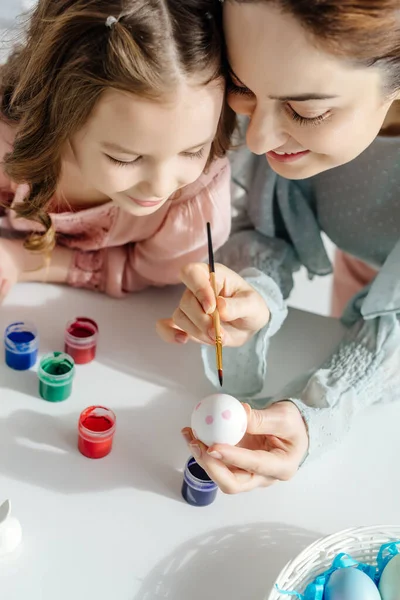 Enfoque selectivo de la madre feliz y alegre hija pintando huevo de gallina - foto de stock