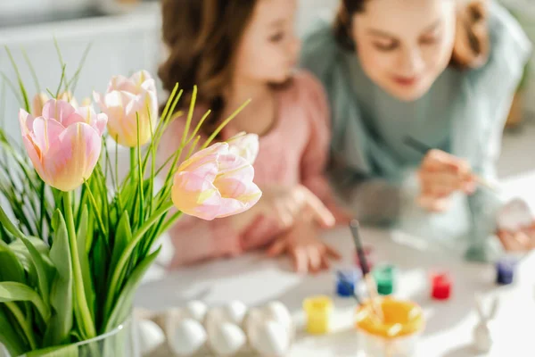 Селективный фокус тюльпанов вблизи матери и дочери, рисующих пасхальные яйца — стоковое фото