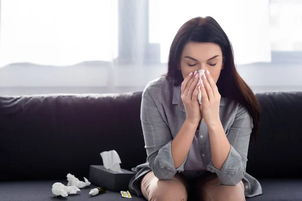 Frau mit Allergie niest in Serviette, während sie auf Sofa sitzt — Stockfoto