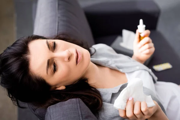 Selective focus of allergic woman holding tissue and nasal spray while sitting on sofa — Stock Photo