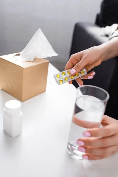 Cropped view of allergic woman holding blister pack with pills and glass of water and tissue box — Stock Photo