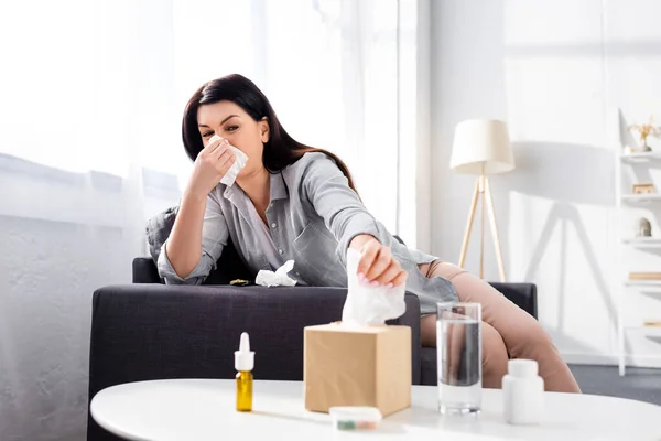 Selective focus of allergic woman with running nose taking napkin near glass of water — Stock Photo