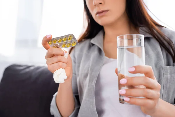 Cropped view of woman holding blister pack with pills and glass of water — Stock Photo