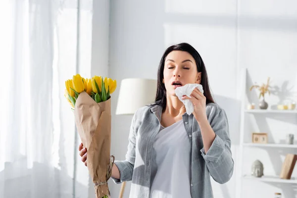 Attractive woman with pollen allergy sneezing while holding tulips — Stock Photo