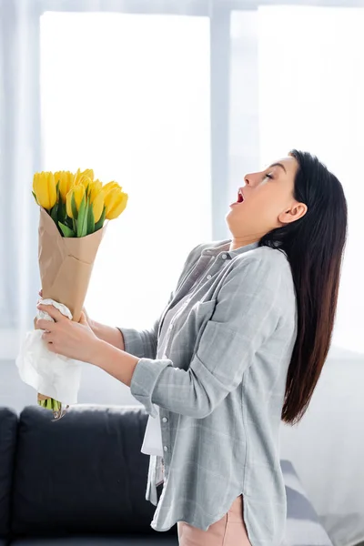 Mujer estornuda con alergia al polen y ojos cerrados sosteniendo tulipanes - foto de stock