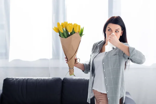 Sneezing woman with pollen allergy looking at flowers — Stock Photo