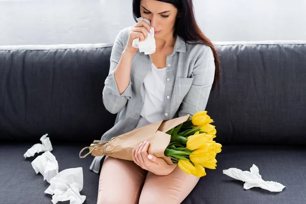 Niesende Frau mit Pollenallergie sitzt auf Sofa mit Blumen — Stockfoto