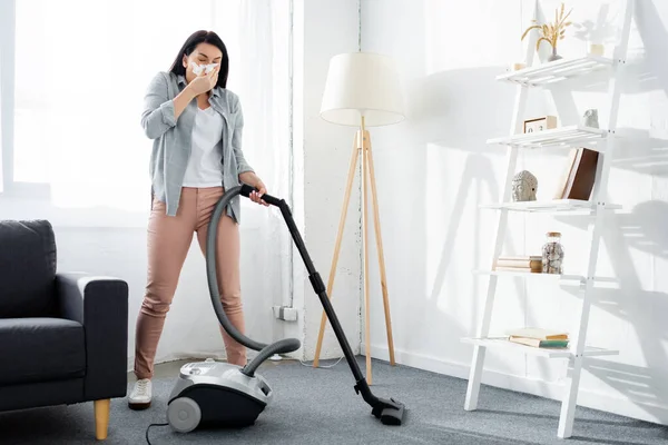 Allergic woman covering mouth with napkin and cleaning modern living room with vacuum cleaner — Stock Photo