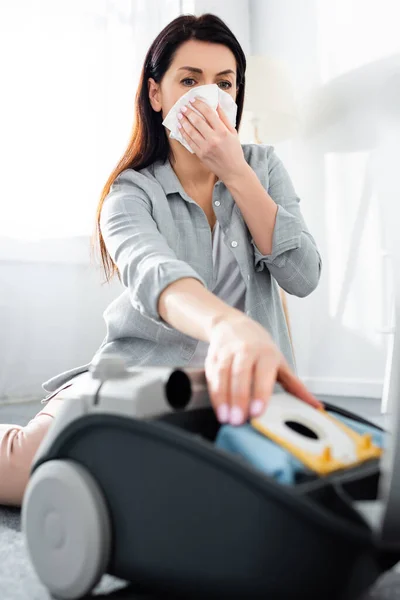 Selective focus of allergic woman covering mouth with tissue and reaching for dust bag in vacuum cleaner — Stock Photo