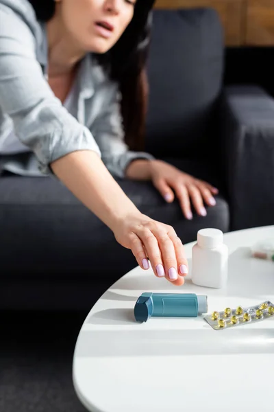 Vue recadrée de la femme atteignant pour inhalateur près de plaquette thermoformée avec des pilules sur la table basse — Photo de stock