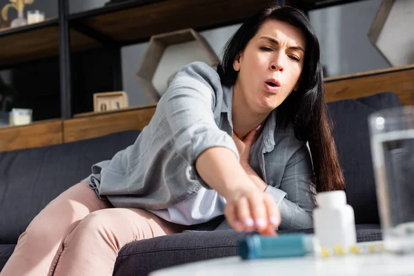 Selective focus of woman with asthma coughing while reaching for inhaler — Stock Photo