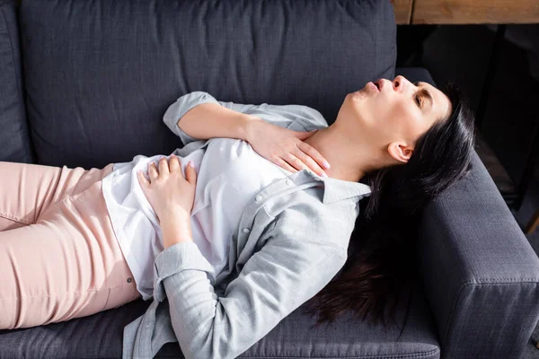 Астматичная женщина кашляет, лежа на диване — стоковое фото