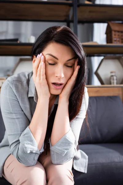 Woman with migraine touching temples while sitting on sofa — Stock Photo