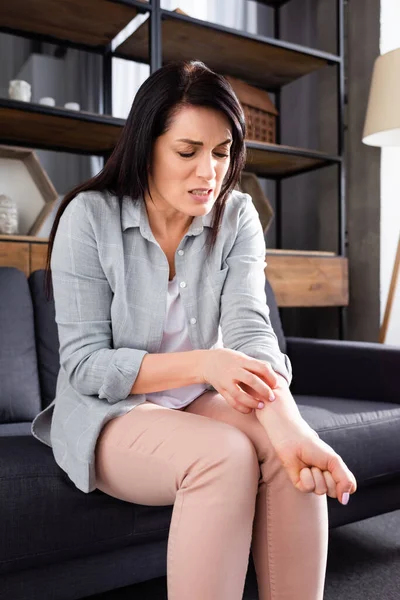 Allergic woman scratching hand while sitting on sofa — Stock Photo