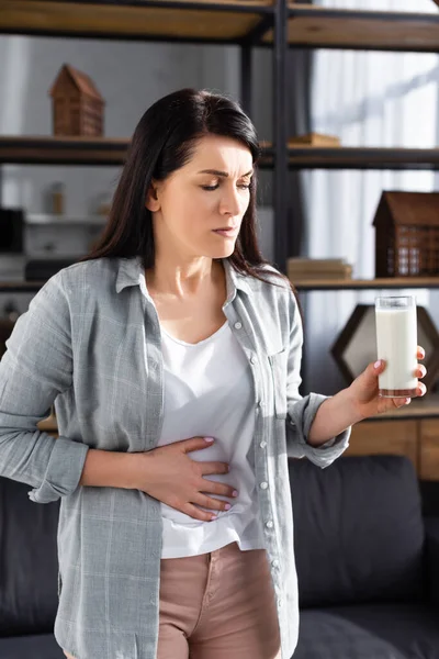 Mujer triste con intolerancia a la lactosa sosteniendo un vaso de leche - foto de stock