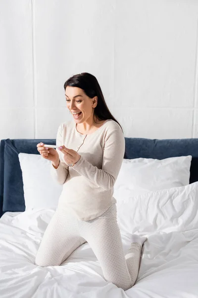 Excited woman holding pregnancy test in bedroom — Stock Photo