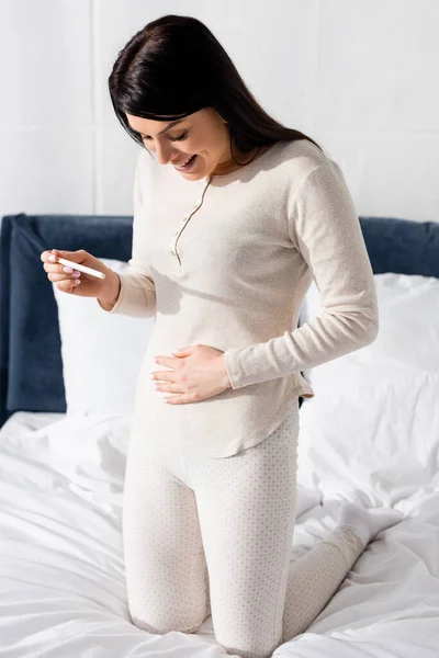 Mujer feliz celebración de la prueba de embarazo en el dormitorio - foto de stock