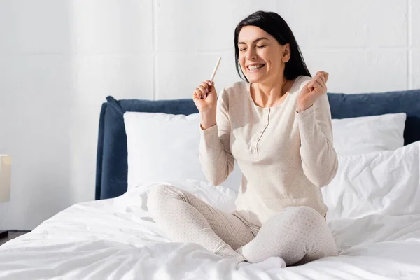 Happy pregnant woman holding pregnancy test in bedroom — Stock Photo