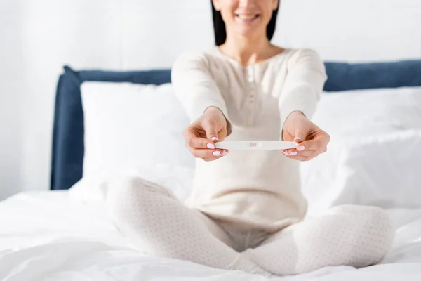 Selective focus of cheerful woman holding pregnancy test in bedroom — Stock Photo