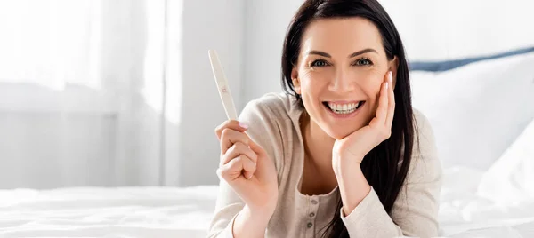 Panoramic shot of cheerful and pregnant woman holding pregnancy test — Stock Photo