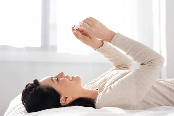 Glückliche Frau lächelt und schaut Schwangerschaftstest an, während sie im Bett liegt — Stockfoto