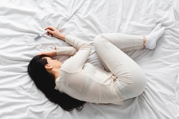 Vista superior da mulher deprimida deitada na cama perto do teste de gravidez com resultado negativo — Fotografia de Stock