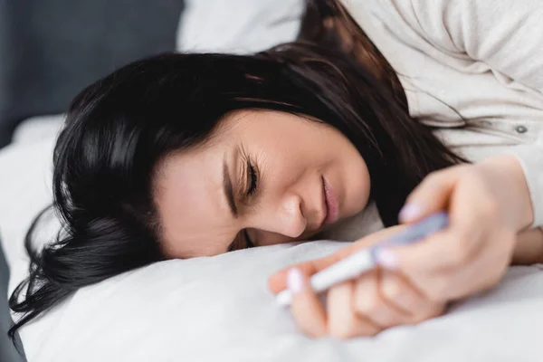 Selektiver Fokus der Frau, die auf dem Bett liegt und Schwangerschaftstest mit negativem Ergebnis hält — Stockfoto