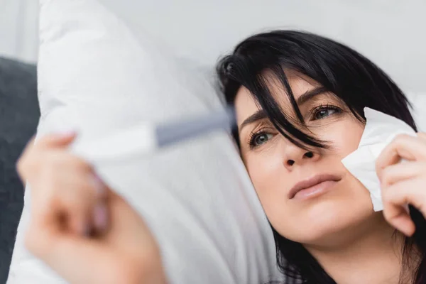 Enfoque selectivo de la mujer molesta mirando la prueba de embarazo con resultado negativo mientras está acostado en la cama - foto de stock