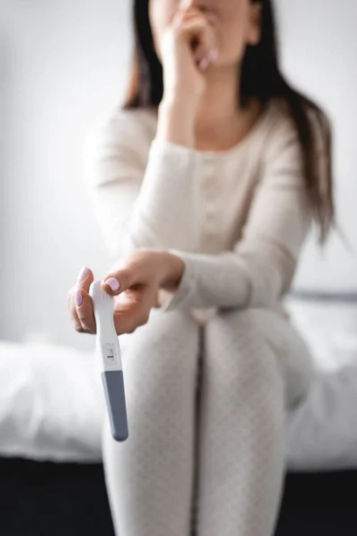 Cropped view of woman sitting on bed and holding pregnancy test with negative result — Stock Photo