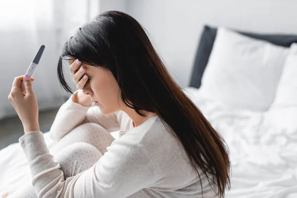 Mujer decepcionada celebración de la prueba de embarazo con resultado negativo en el dormitorio - foto de stock