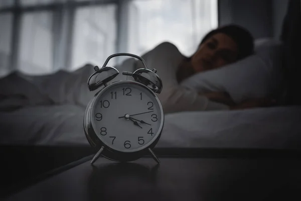 Selective focus of alarm clock on bedside table near awake woman — Stock Photo