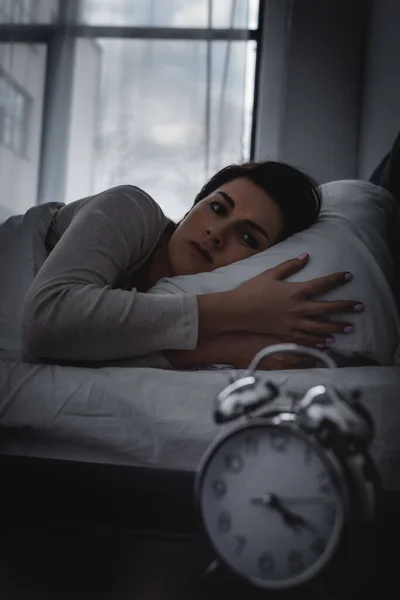 Selective focus of awake woman looking at alarm clock on bedside table — Stock Photo