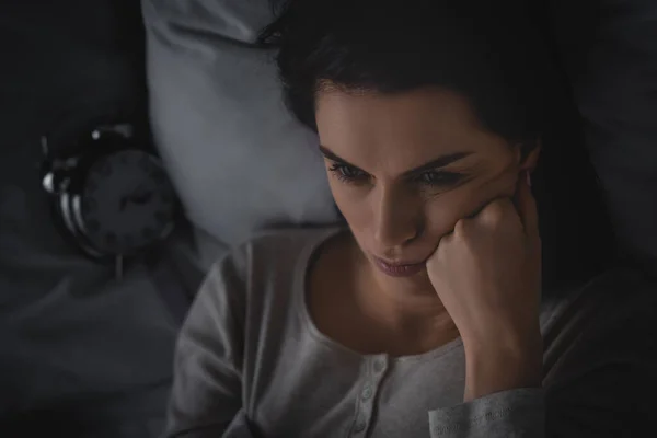 Вид расстроенной женщины с бессонницей лежащей на кровати рядом с будильником — стоковое фото