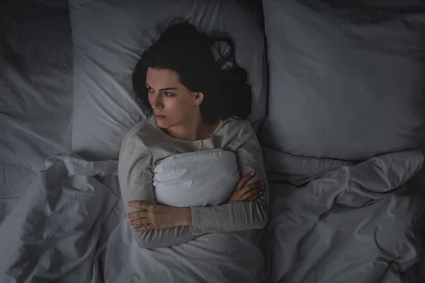 Top view of woman with sleep disorder and crossed arms lying in bedroom — Stock Photo