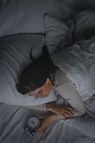 Vista superior de la mujer con trastorno del sueño mirando el reloj despertador en el dormitorio - foto de stock