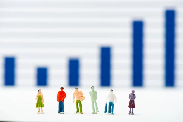 Selective focus of people figures on white surface with infographics at background, concept of equality — Stock Photo