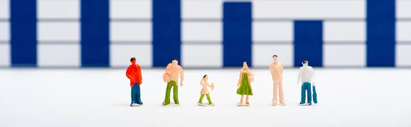Tiro panorâmico de figuras de pessoas de plástico na superfície branca com gráficos azuis no fundo, conceito de igualdade — Fotografia de Stock