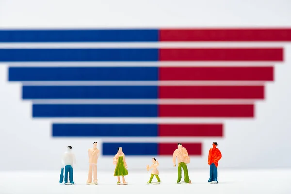 Selective focus of plastic people figures on white surface near blue and red graphs at background, concept of equality — Stock Photo