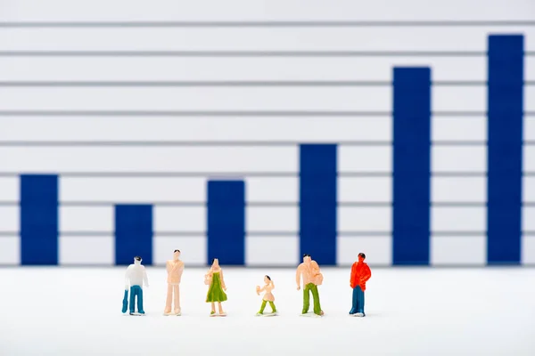 Selective focus of plastic people figures on white surface with blue charts at background, concept of equality — Stock Photo